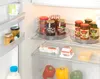 The image shows the inside of a refrigerator with various food items, including jars of jam, cheese, and vegetables. Produktbild-Vorschau