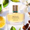 A bottle of Estée Lauder Bronze Goddess perfume surrounded by natural elements like leaves, coconut, lemon, and spices. Anteprima dell’immagine prodotto