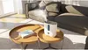 A white humidifier is placed on a round wooden coffee table in a living room, emitting mist. A book is on the same table, and a sofa is in the background. Produktbild-Vorschau