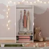 An open wardrobe with clothes and luggage inside, next to a teddy bear. Produktbild-Vorschau
