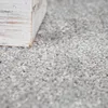 A close-up view of a textured gray carpet with the corner of a distressed white wooden object in the upper left. Produktbild-Vorschau