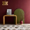 A console table with a lamp and artwork on it, placed on a rug in front of a maroon wall with a green arch. Produktbild-Vorschau