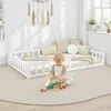 A child plays with a stacking toy on the floor next to a white toddler bed with a guardrail.