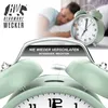 A man sleeping in bed with a green alarm clock in the foreground. Produktbild-Vorschau