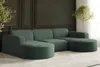 A modern sectional sofa in a dark green corduroy fabric, set against a dark paneled wall with a small tree in the background.