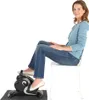 A woman sits on a white chair using a black mini bike pedaltrainer. Produktbild-Vorschau