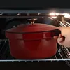A hand is placing a red pot into an oven. Anteprima dell’immagine prodotto