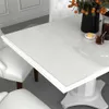A white dining table with a transparent protective film on top, set in a dining room with white chairs. Produktbild-Vorschau