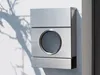 A modern stainless steel mailbox mounted on a white wall, with a shadow of tree branches cast on the wall. Produktbild-Vorschau