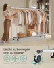 A woman is standing next to a rolling garment rack filled with clothes. The bottom part of the image shows a close-up of a wheel with locking mechanism and text in German. Produktbild-Vorschau