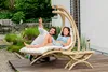 A couple relaxing on a wooden deck in a garden, with a hanging chair and a small side table. Produktbild-Vorschau