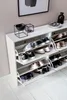A white shoe cabinet with multiple shelves filled with shoes, placed against a light pink wall. Náhled obrázku produktu