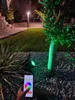 A person is using a smartphone to control a green outdoor smart light in a garden at night. Voir les images du produit