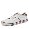 A white canvas sneaker with brown accents and colored stripes on the sole. Produktbild-Vorschau
