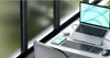 A desk setup with a laptop, keyboard, mouse, and smartphone next to a window. Podgląd zdjęcia produktu