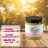 A jar of peanut butter for wild birds is placed on a wooden table with a blurred background of trees and sunlight. Produktbild-Vorschau