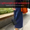 A person is holding a small black speaker with a lanyard, with a brown bag in the background. Produktbild-Vorschau