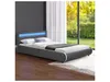 A modern bed with a grey frame and a blue LED headboard is shown in a room with a large window overlooking a garden. Náhled obrázku produktu