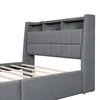 A close-up, angled view of a grey upholstered bed frame with a headboard that has built-in storage compartments and LED lighting. Náhľad obrázku produktu
