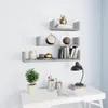 Three gray U-shaped shelves mounted on a white wall, decorated with various items including books, a clock, a plant, and decorative objects. A desk with a lamp and more decorative items is visible at the bottom. Náhľad obrázku produktu