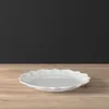 A white decorative plate is placed on a wooden table against a black background. Voir les images du produit