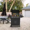 A gas grill is set up on a paved patio in a backyard, with a table and chairs nearby and a garage in the background. Podgląd zdjęcia produktu