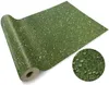 A roll of green ground cover with small white flowers, resembling grass, is shown on a white background. A circular inset shows a close-up of the ground cover. Produktbild-Vorschau