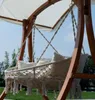 A hammock chair with pillows hanging from a wooden frame, outdoors on a sunny day. Produktbild-Vorschau