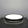 A circular LED ceiling light with a black rim sits on a dark surface against a light gray background. Produktbild-Vorschau