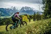 A person riding a mountain bike on a grassy slope with mountains in the background. Náhľad obrázku produktu