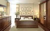 A bedroom scene featuring a large wooden wardrobe with mirrored doors, a bed, and other furniture. Produktbild-Vorschau
