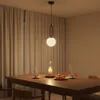 A dining table set with cups, fruit, and a candle under a glass dome, illuminated by a modern pendant light. Náhled obrázku produktu