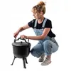 A woman is crouching next to a cast iron pot with legs. Podgląd zdjęcia produktu