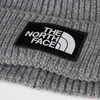 A close-up shot of a gray knitted beanie with a black patch featuring the white North Face logo. Produktbild-Vorschau