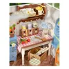 A miniature dollhouse scene depicting a crafting or gardening area with shelves, a table, and various accessories. Anteprima dell’immagine prodotto
