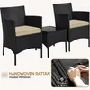 A black rattan furniture set with beige cushions, including two chairs and a small table, against a white background. A close-up inset shows hands weaving rattan. Produktbild-Vorschau