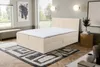 A bedroom scene featuring a beige boxspring bed with storage drawers, a patterned rug, and decorative elements. Voir les images du produit