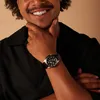 A man wearing a black shirt and a watch, with his hand on his chin. Produktbild-Vorschau
