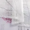 A close-up view of a sheer curtain with a floral pattern, layered over a magazine or book. Produktbild-Vorschau