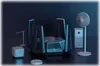A collection of smart home devices, including a router, air purifier, fan, desk lamp, and robot vacuum, arranged on a dark surface. Podgląd zdjęcia produktu