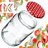 A clear glass jar with a red and white polka dot lid, surrounded by fresh vegetables and herbs. Voir les images du produit
