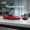 A red toy car model is displayed on a table next to a small screen showing a picture of the same car. Anteprima dell’immagine prodotto