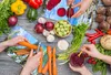A top-down view of a collection of fresh vegetables and hands preparing them, with images of a waterfall scene as placemats. Produktbild-Vorschau