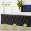 A close-up view of a black upholstered boxspring bed with a white topper, featuring LED lighting in the headboard and promotional icons at the bottom. Produktbild-Vorschau