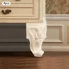 A close-up view of a carved wooden furniture leg with a rose design, attached to a cream-colored cabinet. The background shows a wall with patterned wallpaper and molding. Podgląd zdjęcia produktu