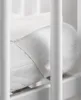 A close-up view of a white mattress protector with a quilted pattern and an elastic strap, seen through the white bars of a crib. Produktbild-Vorschau