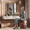 A woman is applying makeup in front of a vanity table. Produktbild-Vorschau