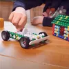 A child's hands are building a toy car and a house with colorful building blocks on a wooden table. Produktbild-Vorschau