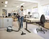 A woman is vacuuming an office floor with a commercial vacuum cleaner. Produktbild-Vorschau