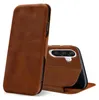 A brown leather flip case for a smartphone is shown against a white background. The case is partially open, revealing the back of a smartphone with a triple camera setup. Anteprima dell’immagine prodotto